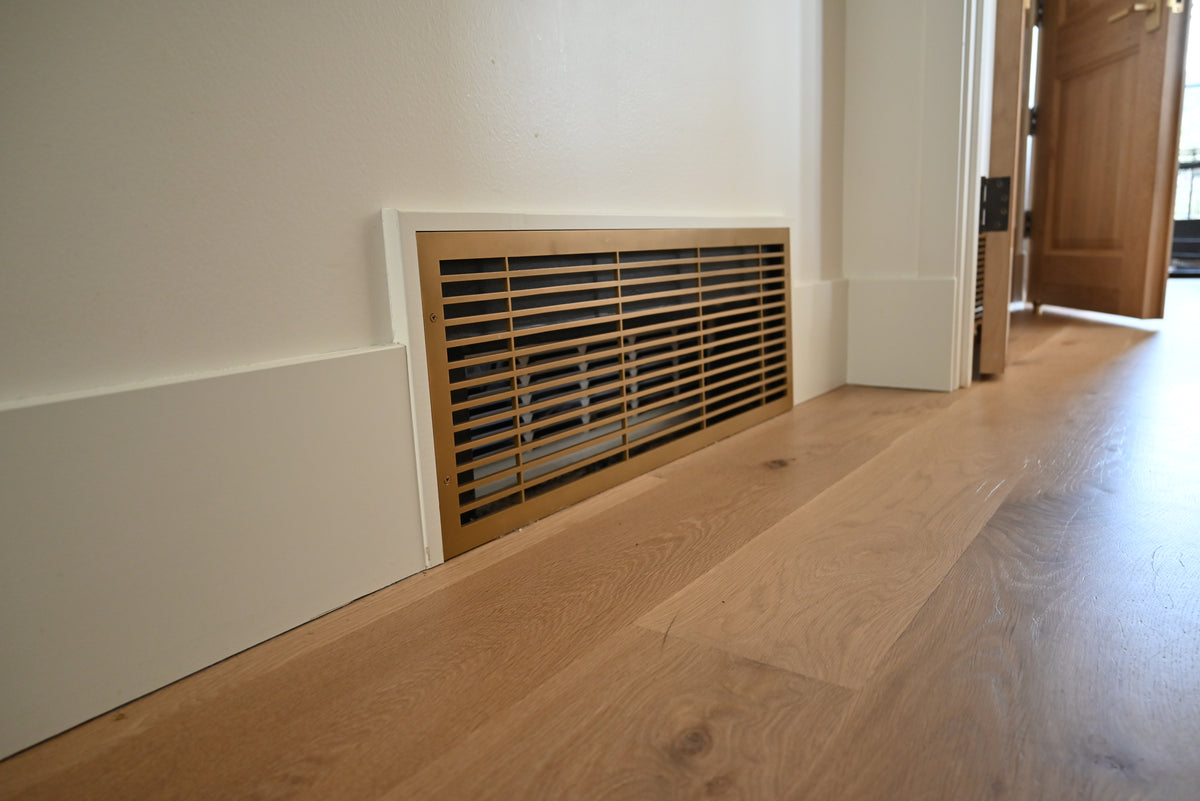 Modern linear baseboard air return made out of metal with a white oak floor and tall baseboards.