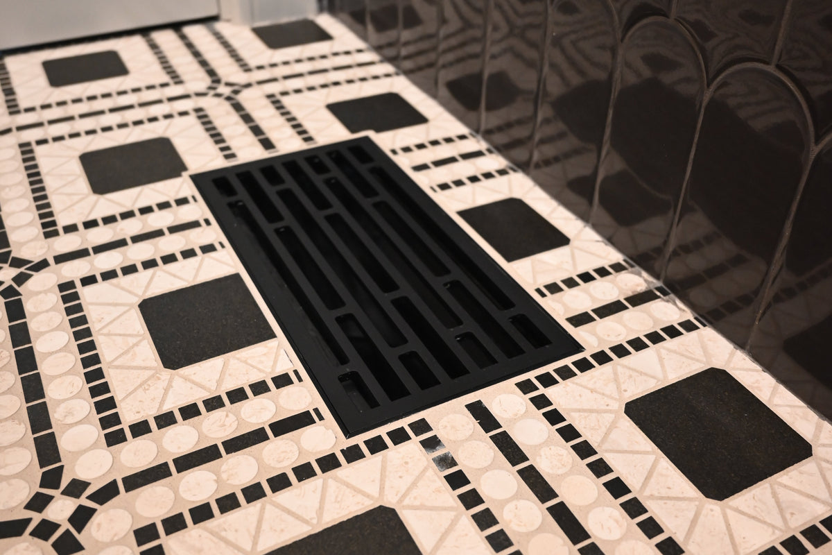 Straight - tile flush mount vent - matte black. A black rectangular flush vent set into a black and white geometric mosaic tile floor, with a dark reflective surface in the background.