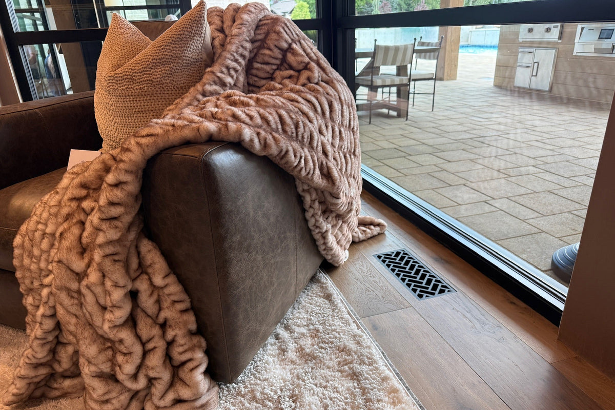 A steel decorative flush mount vent into a hardwood floor next to a leather arm chair with a Minky blanket next to an outdoor patio with a pool.